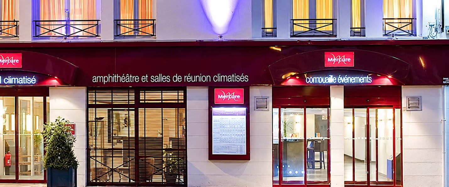 Entrées de l’hôtel Mercure en soirée, avec enseignes lumineuses et vitrines éclairées.